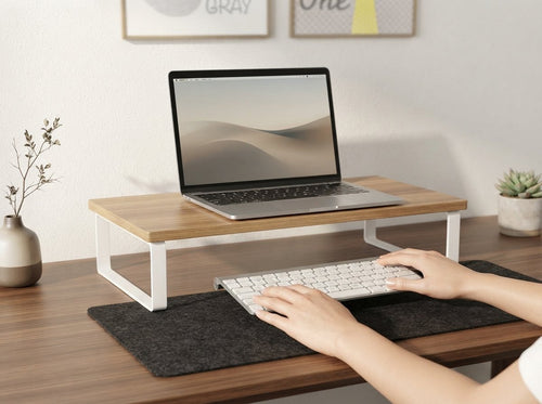 Hands placing a keyboard beneath the Ergora Bench monitor riser with a laptop resting on top